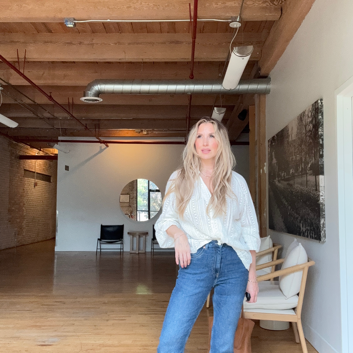Quinn wearing blue jeans and a white long sleeve shirt in a bright natural light warehouse room