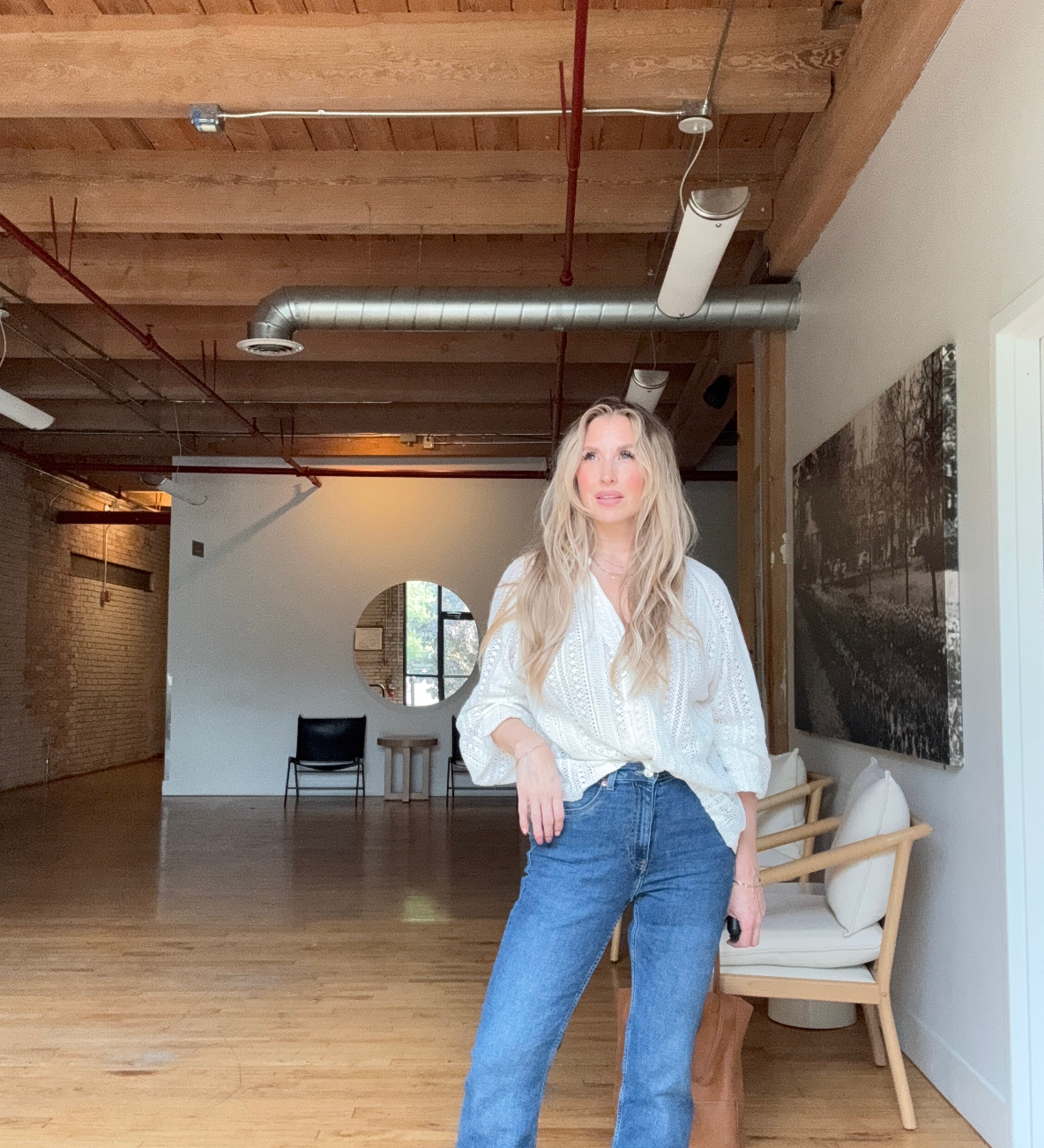 Quinn wearing blue jeans and a white long sleeve shirt in a bright natural light warehouse room