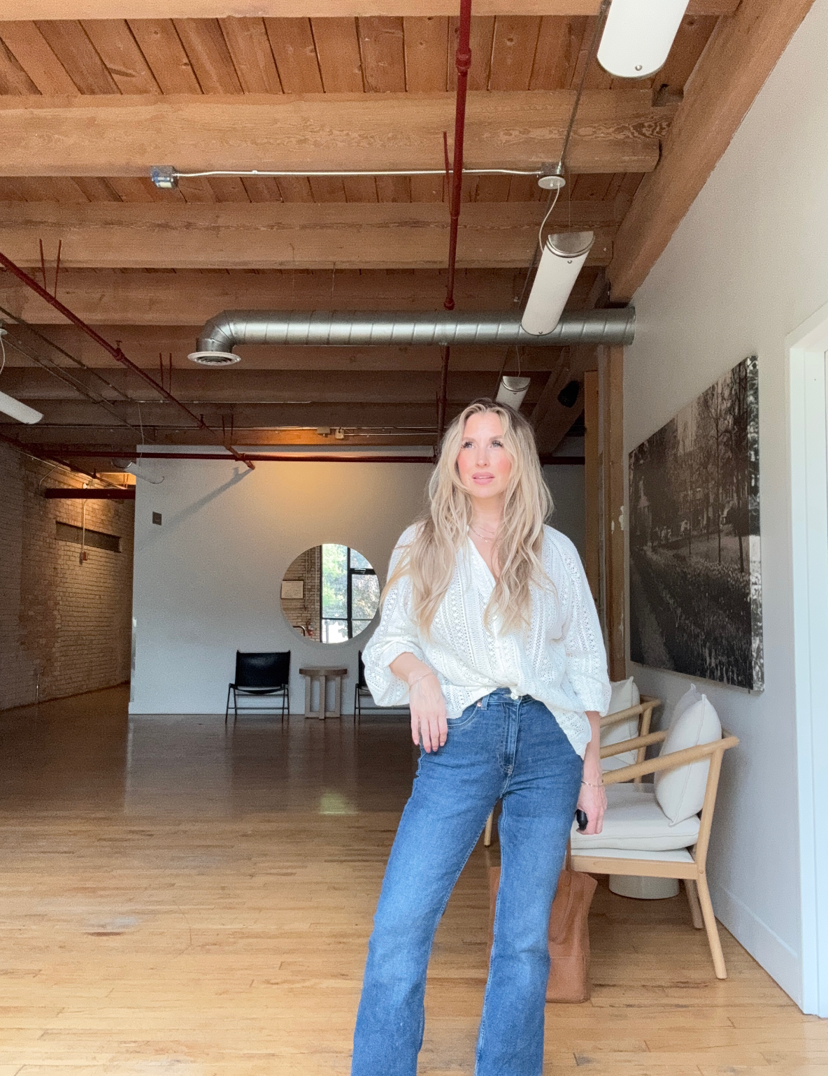 Quinn wearing blue jeans and a white long sleeve shirt in a bright natural light warehouse room