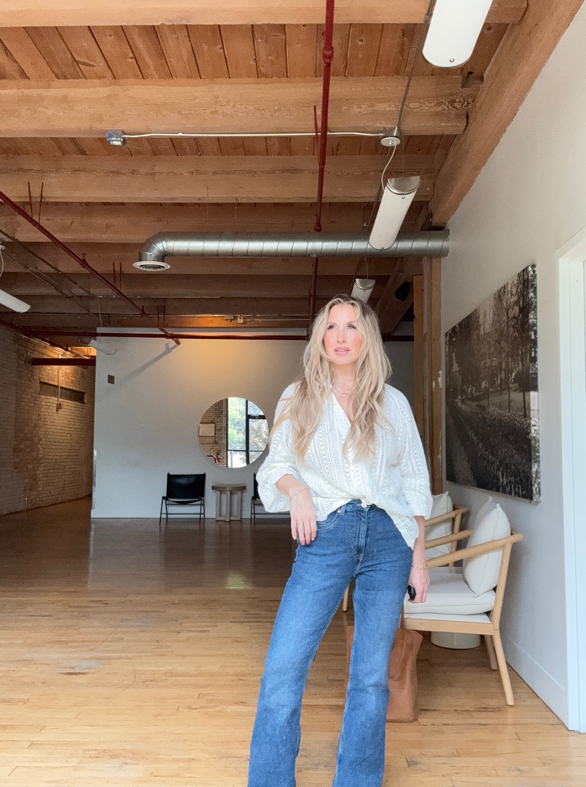 Quinn wearing blue jeans and a white long sleeve shirt in a bright natural light warehouse room