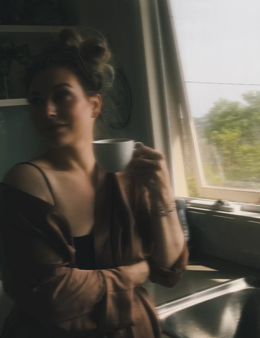A blurry photo of Quinn in a kitchen smiling and holding a mug of coffee