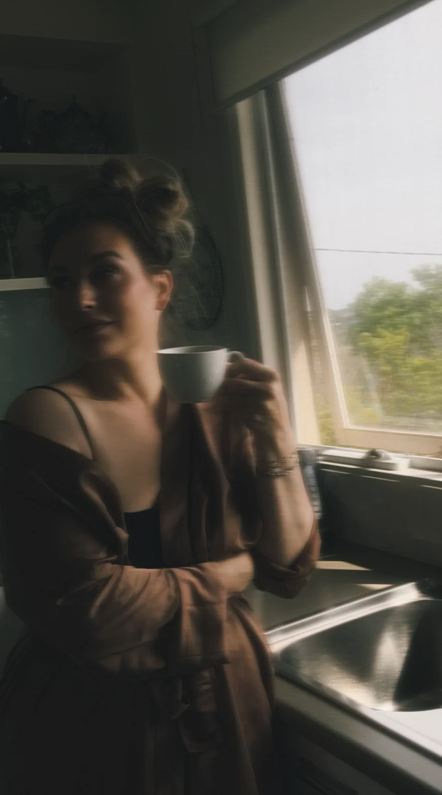 A blurry photo of Quinn in a kitchen smiling and holding a mug of coffee
