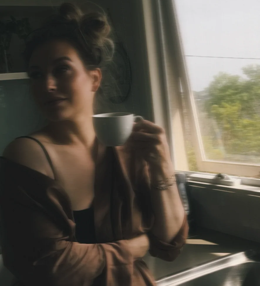 A blurry photo of Quinn in a kitchen smiling and holding a mug of coffee